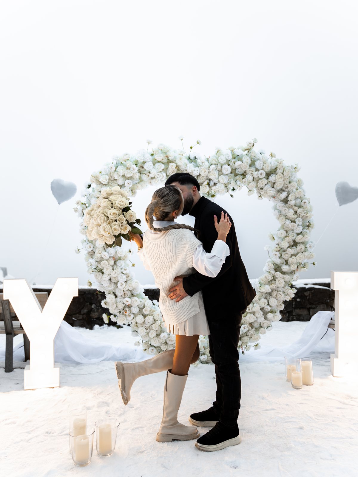 Couple embracing in front of a white rose heart after the proposal