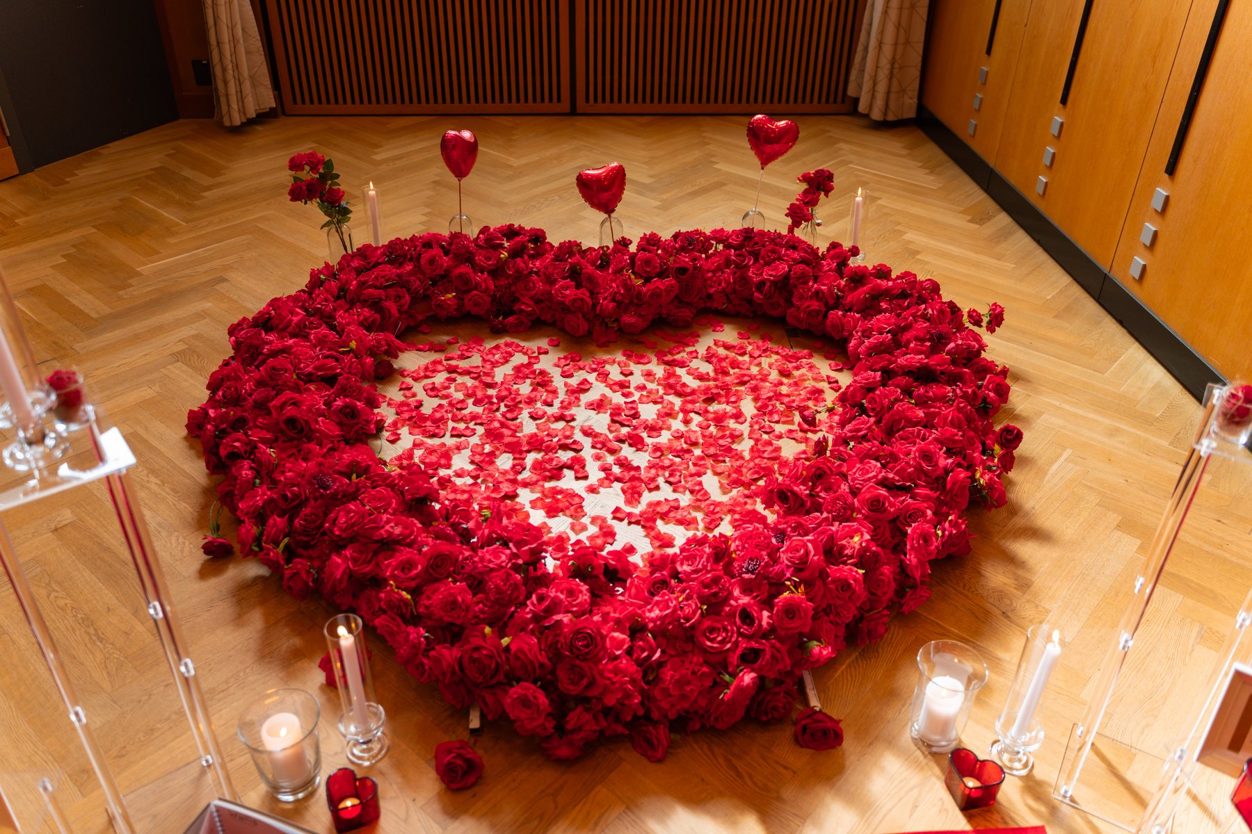Large heart of red roses laid out on a hotel floor with candles