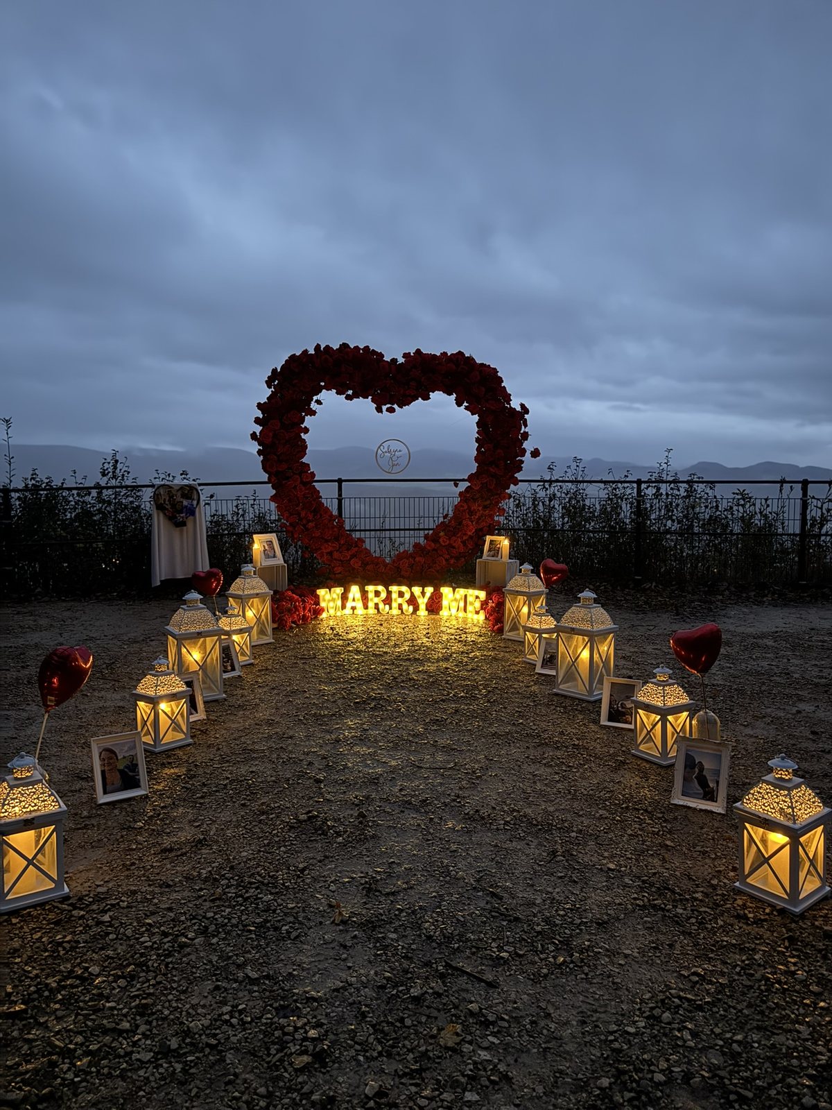 Lantern-lit proposal setup with an illuminated Marry Me sign at dusk